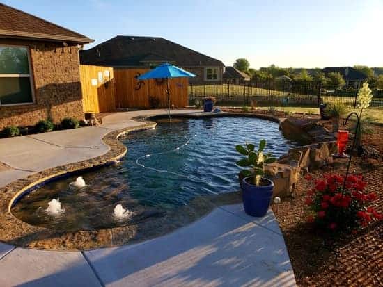Freeform Pool Leichtle Job Freeform pool with an umbrella table and three bubblers surrounded by landscaping and an iron fence