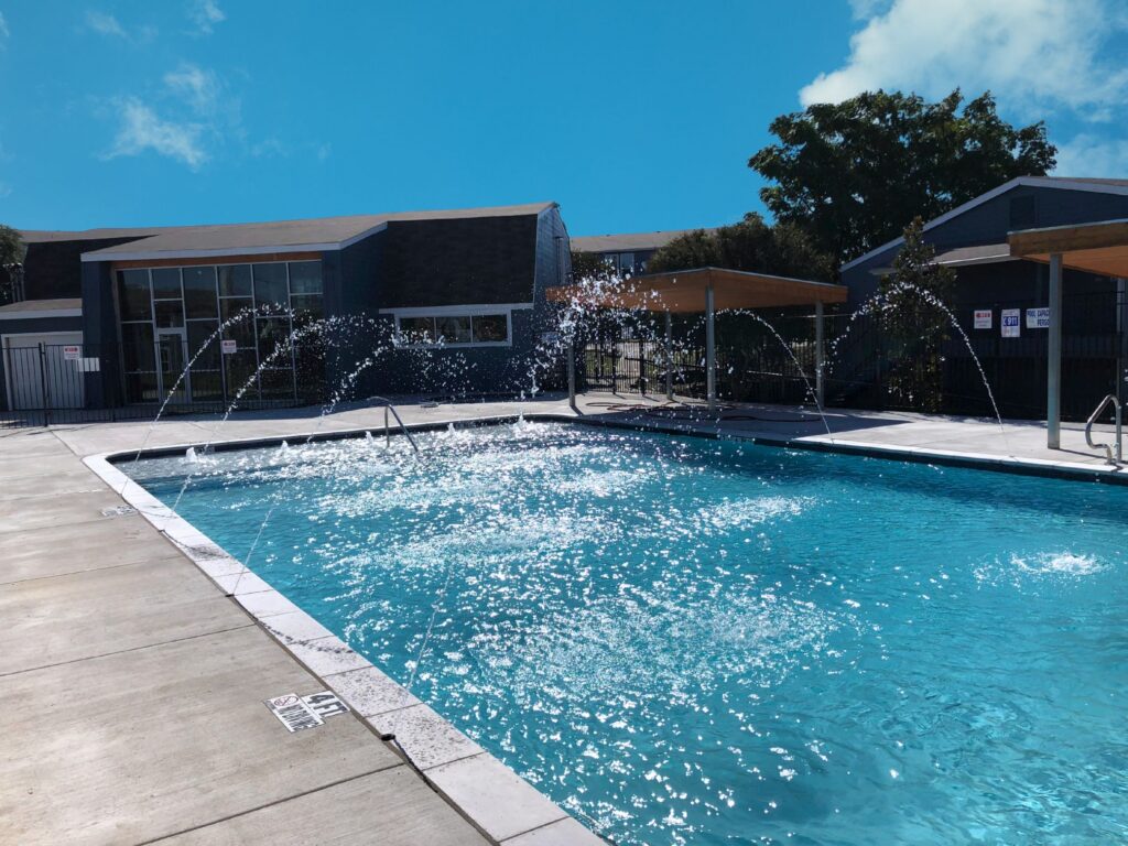 Raised spa and swimming pool with water jets, lounge chairs, and a contemporary stone patio next to a wooden privacy fence.