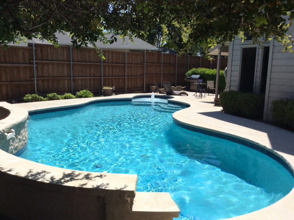 Massive custom inground pool with a stone-clad retaining wall, integrated sun shelf, and multi-level patio transitions overlooking a wooded landscape.