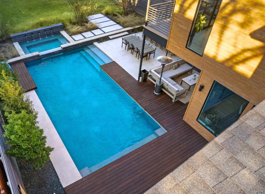 Massive custom inground pool with a stone-clad retaining wall, integrated sun shelf, and multi-level patio transitions overlooking a wooded landscape.