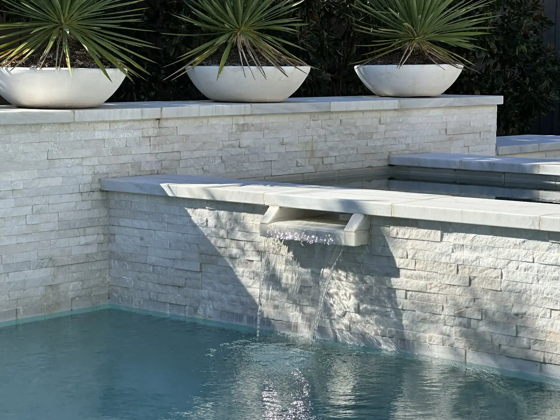 Detailed view of a tiered white stone water feature wall with three integrated planter bowls and a precision water spillway.
