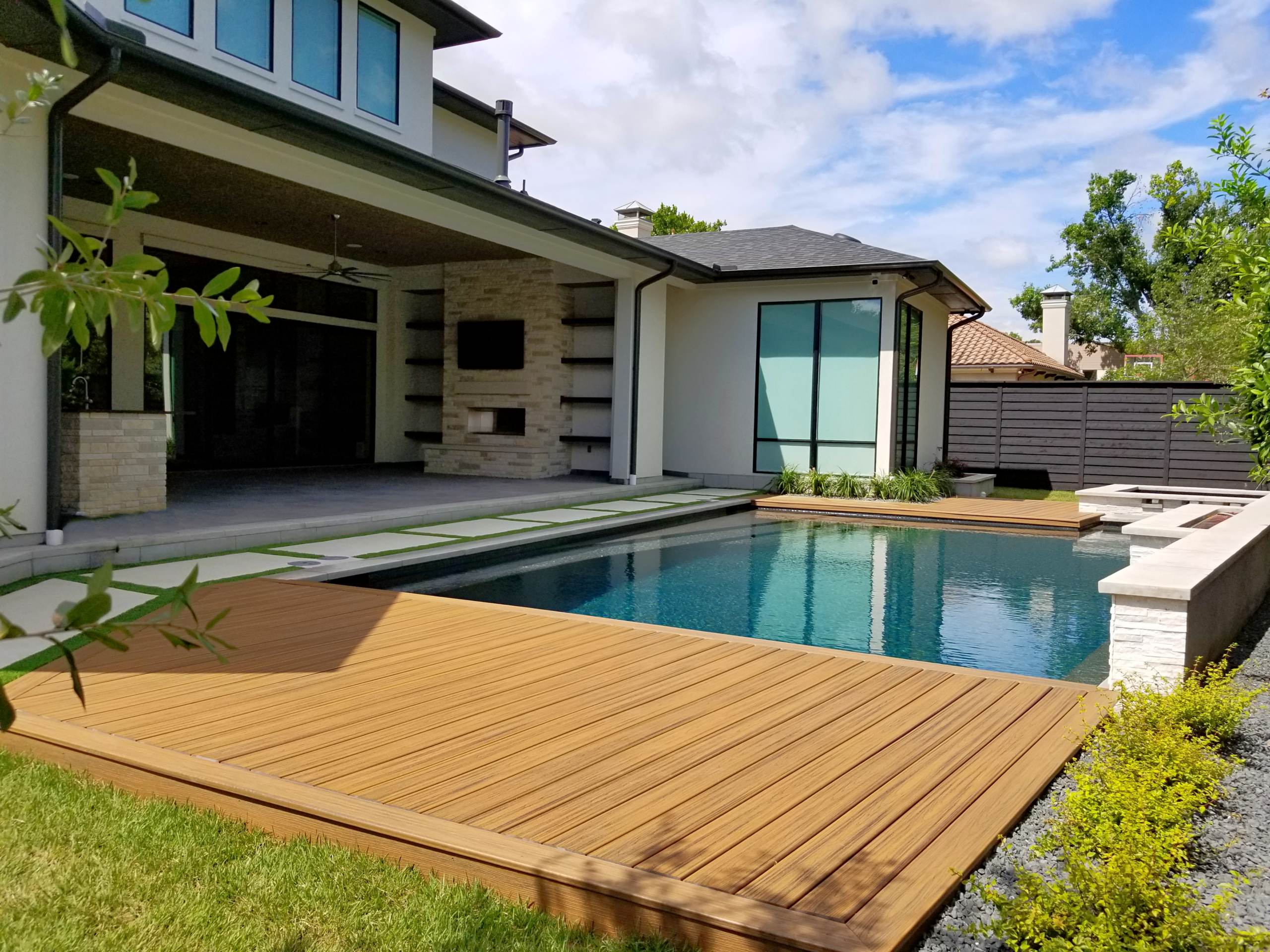 Contemporary geometric pool with a vanishing edge, integrated stone spa, and expansive flagstone decking that blends into a lush, wooded backyard.