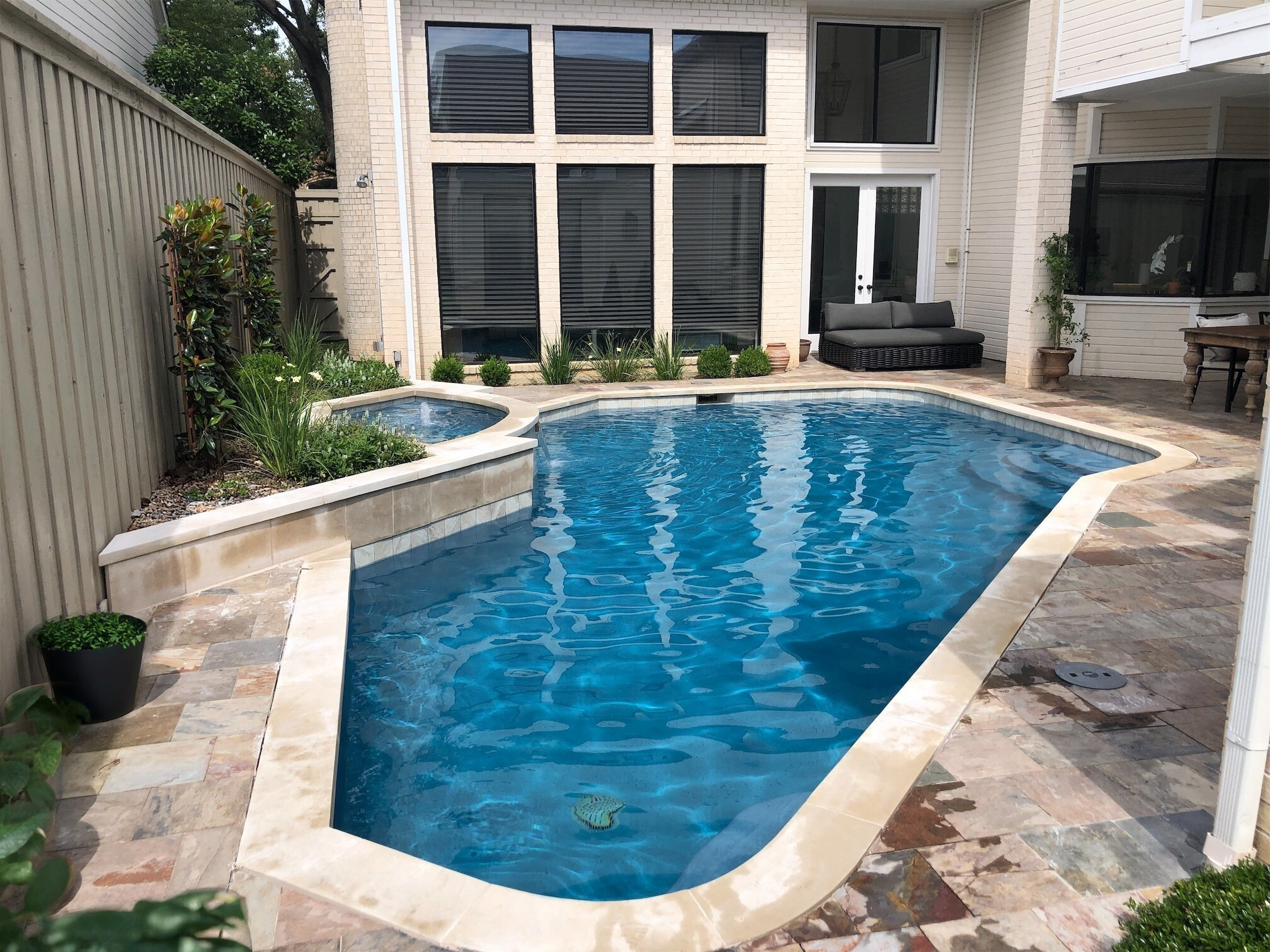 Compact geometric pool design in Dallas, TX, featuring a raised stone spa, integrated garden planters, and a multi-colored slate patio bordering a white brick contemporary home.