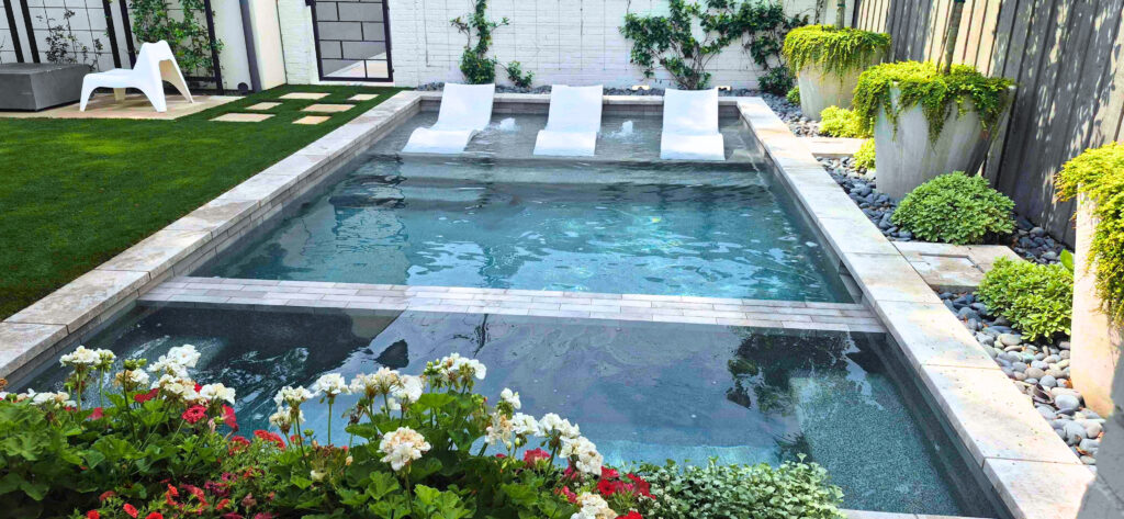 A tiered pool with deep blue mosaic tile accents, integrated sun shelf with umbrellas, and large-scale stone steps.