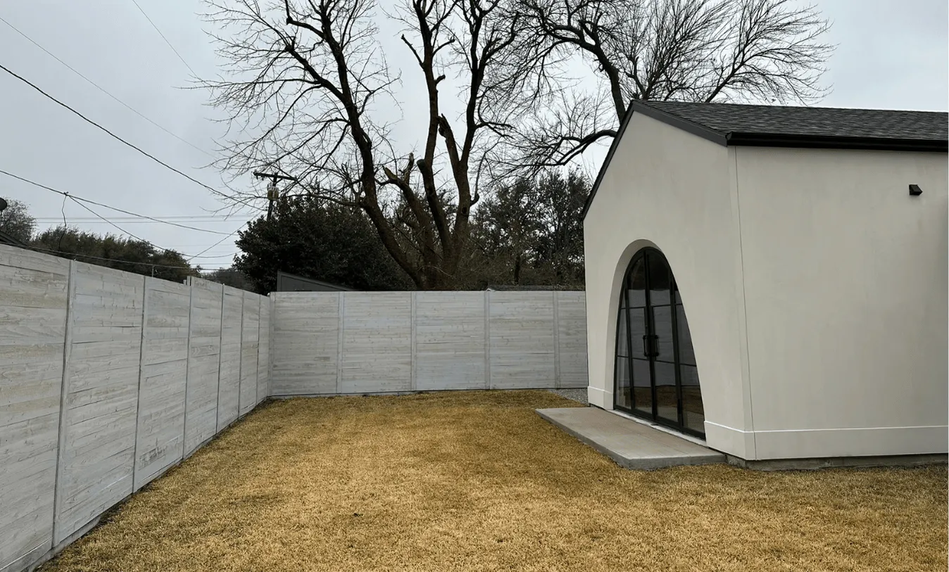 Side view of a white contemporary house with a grey wood-grain concrete fence and a pea-gravel side yard.
