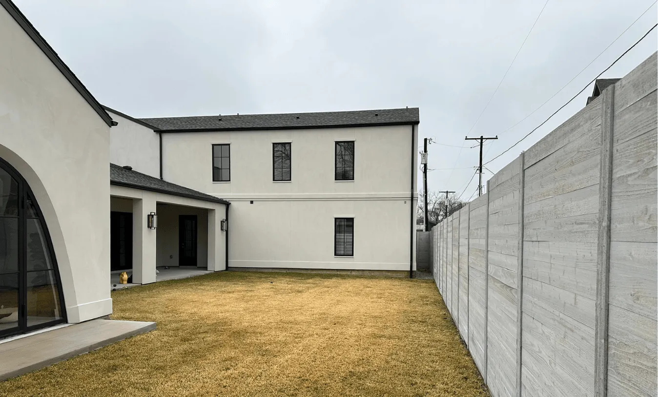 Modern farmhouse exterior with clean white stucco, black-framed windows, and a concrete privacy fence before pool installation.
