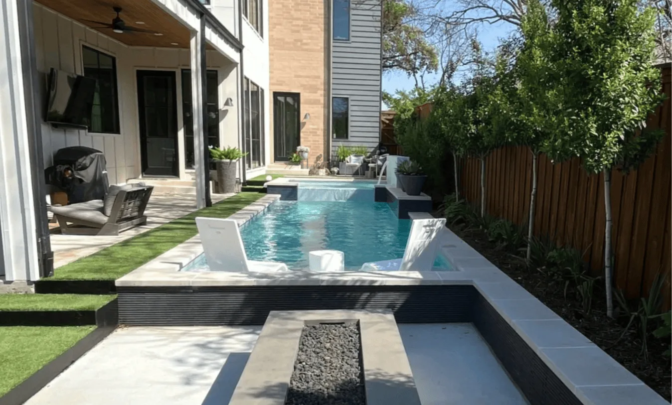 Clean lines in a modern side yard with lush green turf, wood privacy fencing, and large windows reflecting a bright, open outdoor space.