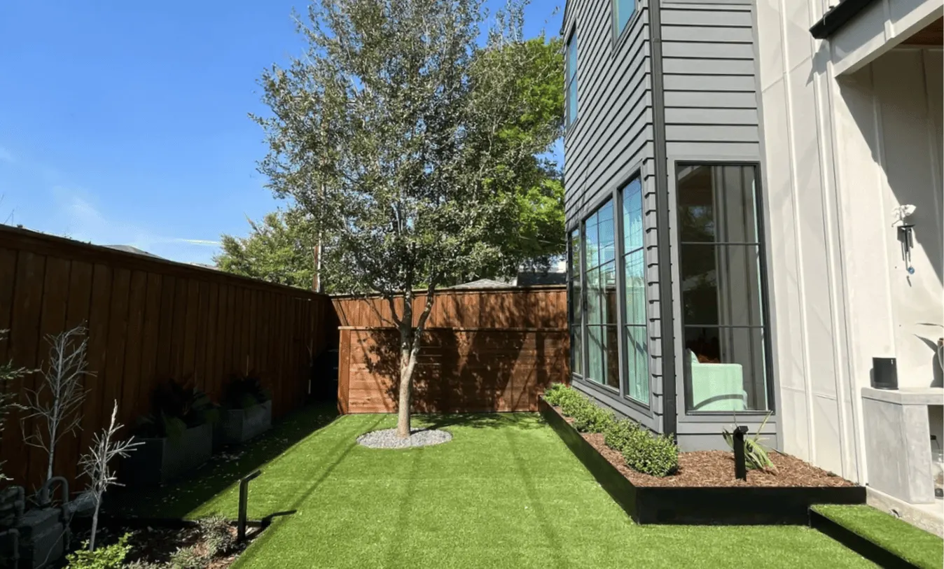 Low-maintenance backyard design with high-quality synthetic grass, a central shade tree, and minimalist landscaping borders.