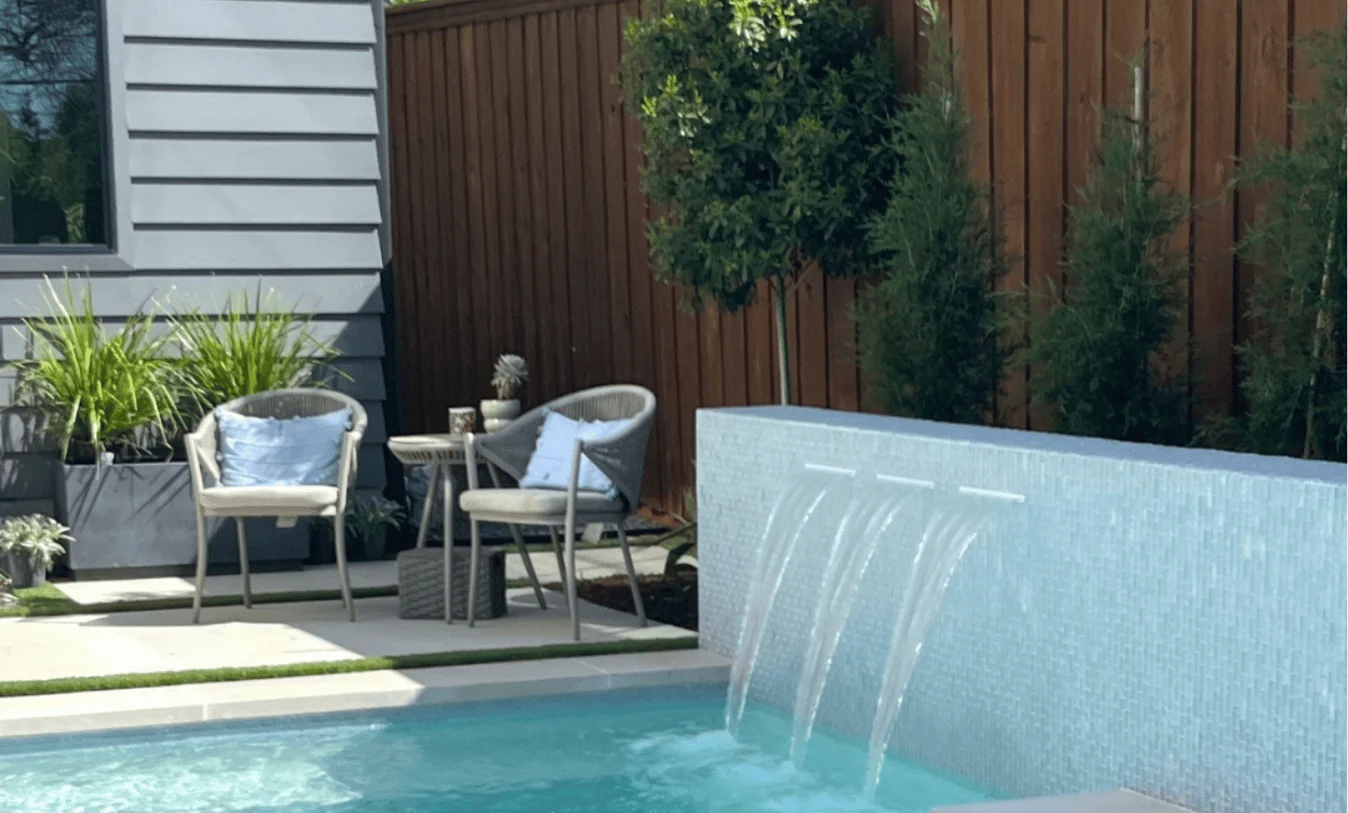 Tiled retaining wall with waterfalls next to a lap pool and modern farmhouse style covered patio.