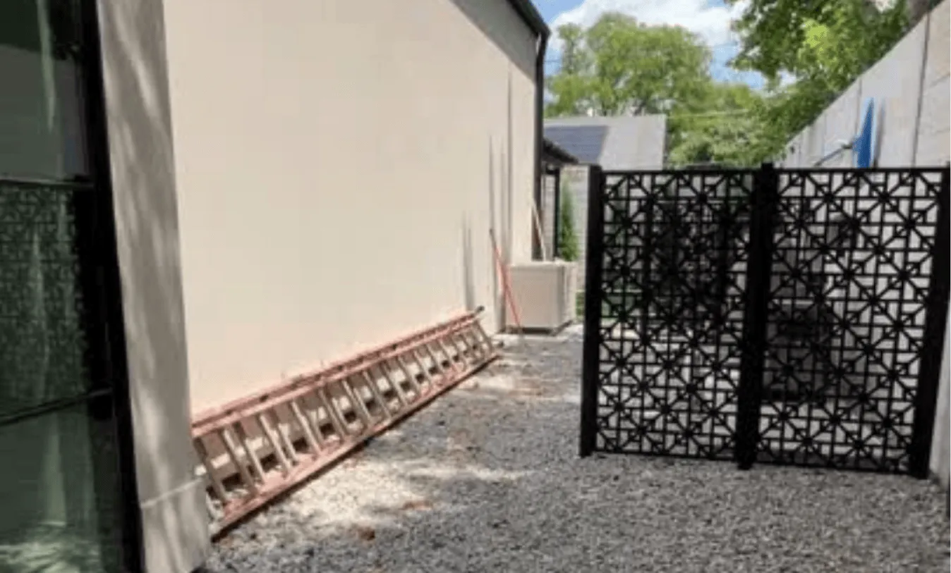 Decorative black metal privacy gate used to hide pool pumps and AC units, matching the modern architectural style of the home and side yard.