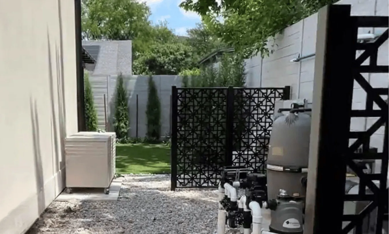 Corner view of a blue mosaic tiled pool and stone deck with privacy hedging and decorative plantings.