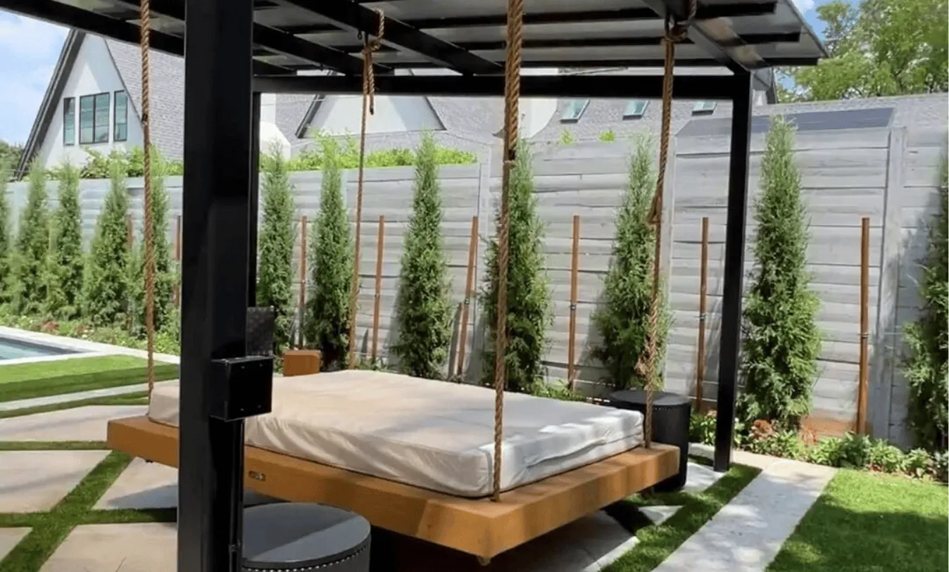 High-end outdoor lounge area with a suspended wooden daybed, modern black pavilion, and decorative concrete pavers with artificial turf inlays.