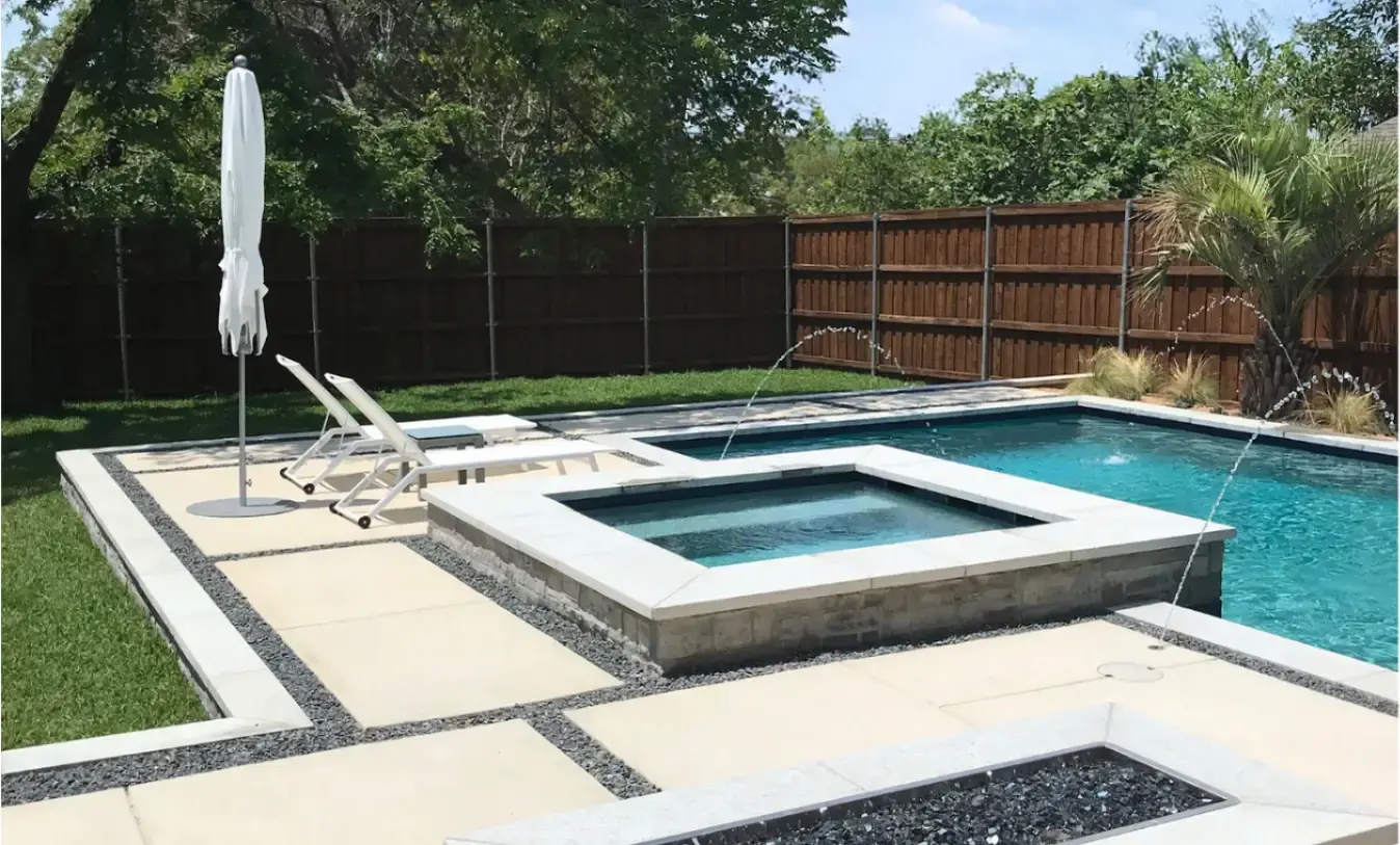 Custom inground pool with a raised stone spa, deck jet water features, and a modern paver patio with charcoal gravel inlays in Arlington, Texas.