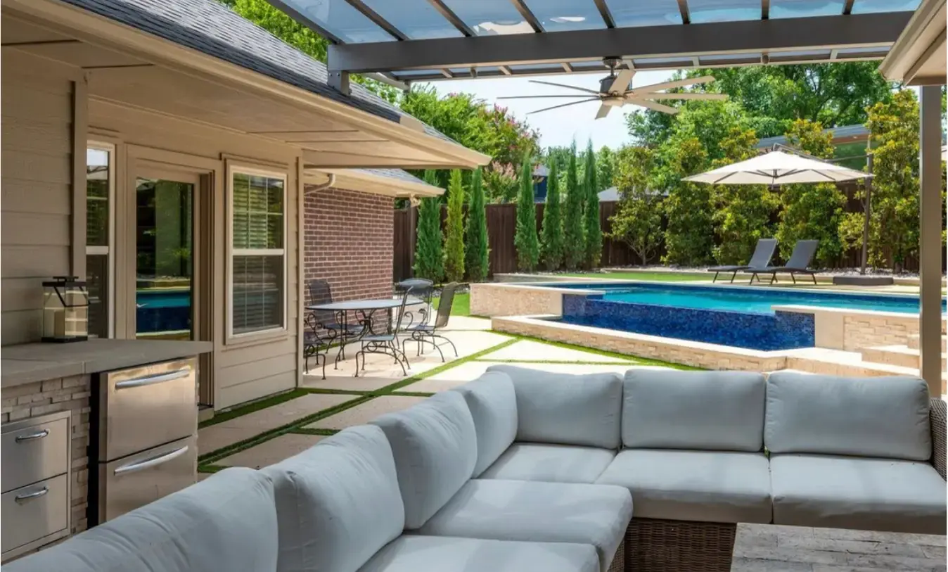 Raised spa and swimming pool with water jets, lounge chairs, and a contemporary stone patio next to a wooden privacy fence.