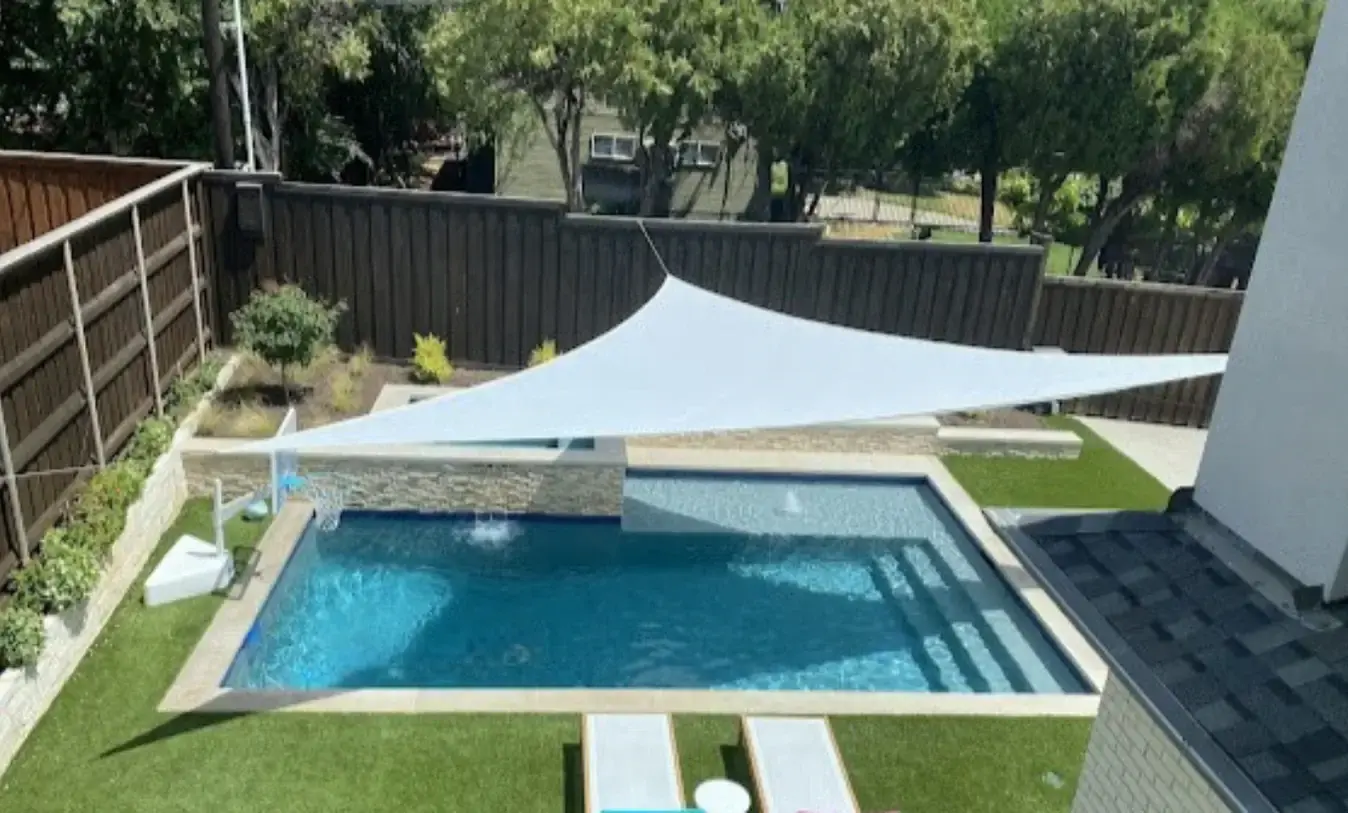 Modern geometric pool design featuring a central square hot tub, arching water fountains, and a tan stone deck with minimalist landscaping.