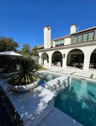 Contemporary pool patio design showcasing white stone pavers separated by vibrant synthetic turf, paired with matching white poolside chairs and minimalist planters.